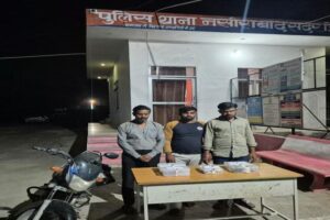 Three accused standing behind a table of recovered jewellery in front of Nasirabad Sadar police station, with a motorcycle beside them